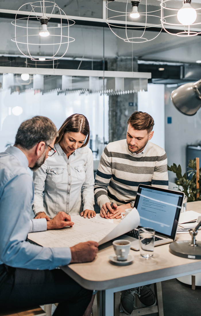 Zwei Männer und eine Frau sitzen zusammen am Bürotisch und planen